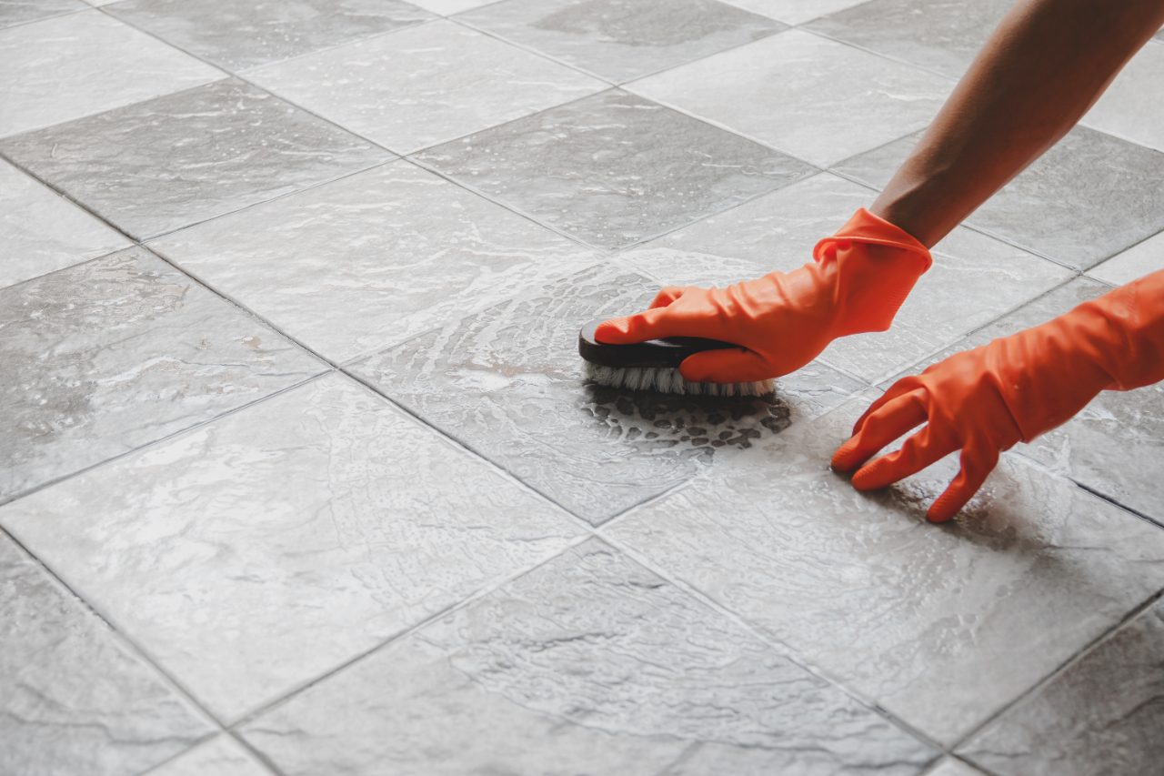 Person in orange gloves scrubbing wet tile floor with brush