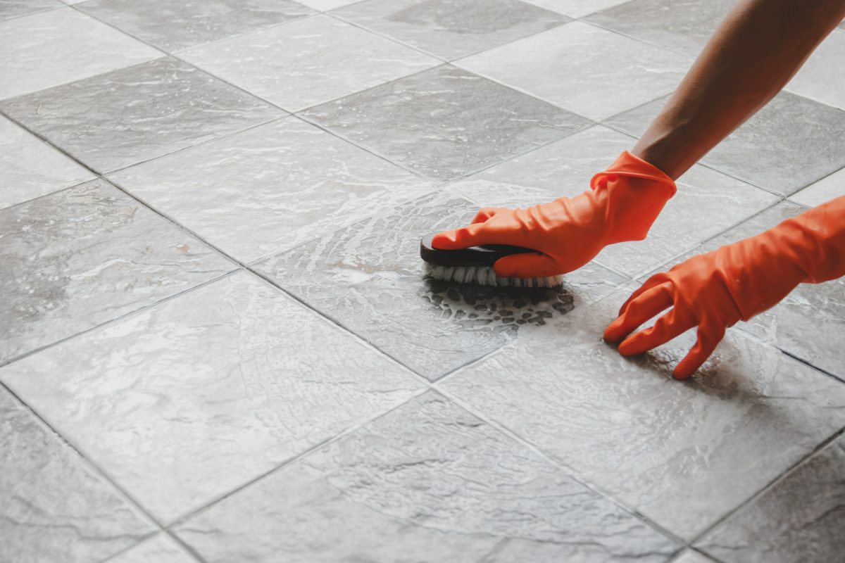 Person in orange gloves scrubbing tile floor with brush